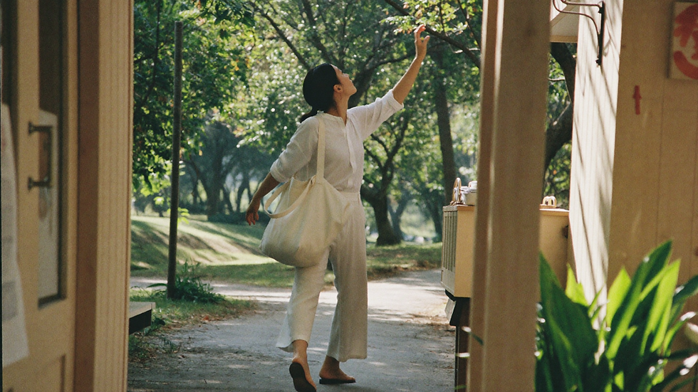 A woman walks with an easy stride down a tree-lined path in the morning, light falling through the leaves