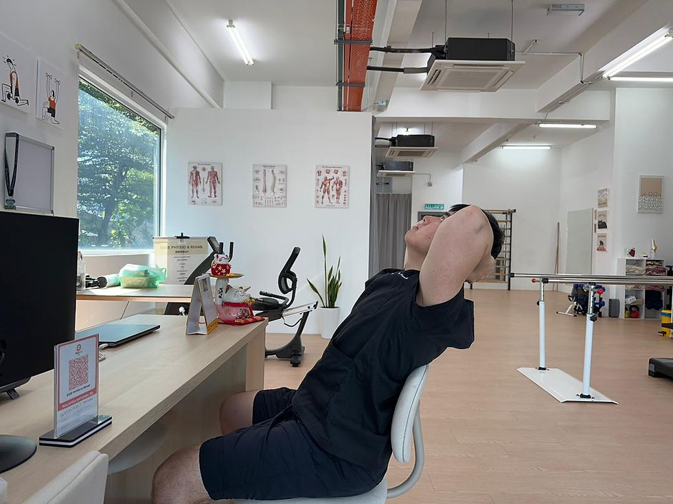 Man doing a backbend on a chair in a bright room with white curtains and plants. Sunlight streams through the large windows.