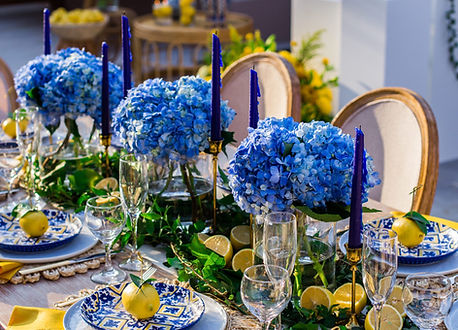 Amalfi-inspired birthday tablescape featuring blue hydrangea centrepieces, blue-and-white Mediterranean tableware, fresh lemons, blue candles and elegant outdoor dining styling.