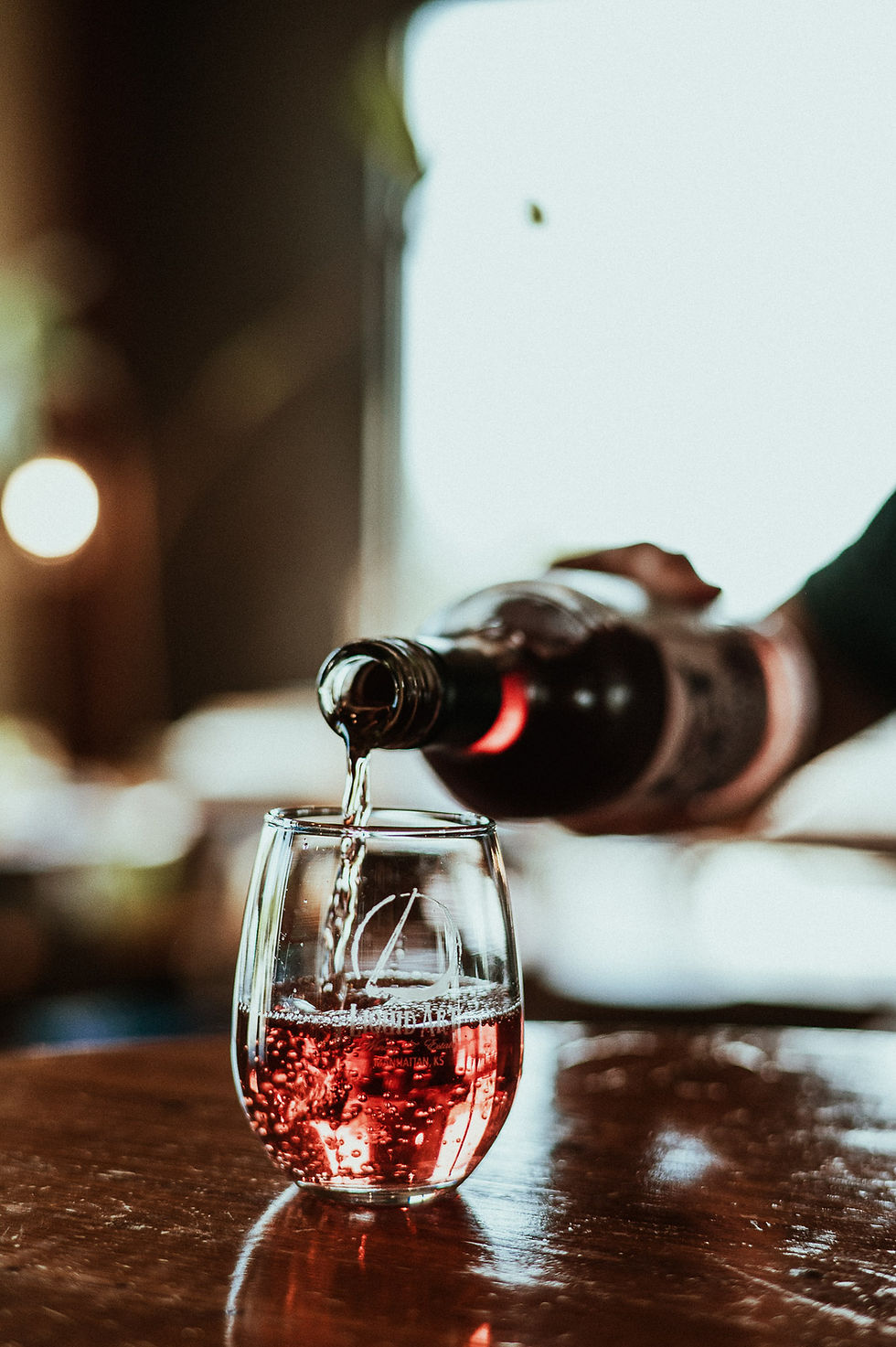 A bottle of wine is pouring a rose wine into a glass.
