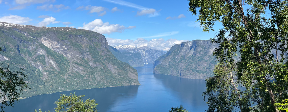 Udsigt over norske bjerger der tårner op fra den klare stille sø. Himlen er blå og luften er klar.