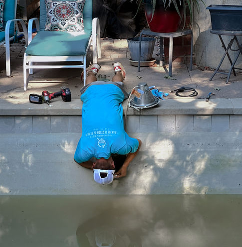 TPB technician laying upside down over the edge of a pool to access and repair a light fixture.