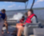 An average height man on a boat wearing a life vest and holding a stress ball. He is smiling with headphones in his ear.