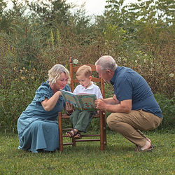 Grandparents (grandmother, grandfather) reading to their young grandson in a field of wildflowers