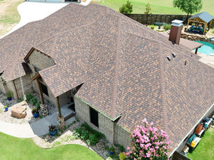 Above view of a house with beige brick and a brown roof with a pool in the backyard