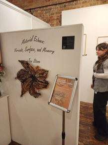 Entrance to Jen Stone's exhibition with wall decal "Material Echoes" sign and brown textured fabric flower.