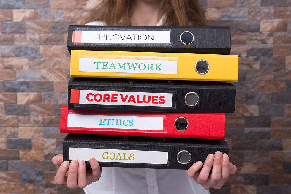 An employee stands with a stack of binders with competing priorities written on the bindings like "Innovation", "Ethics", "Goals", "Core Values", and "Teamwork".