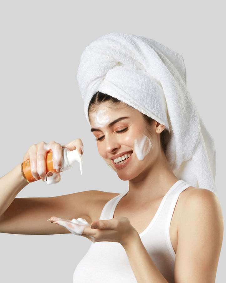 A woman in a towel holds a bottle of Foam Face Wash, 