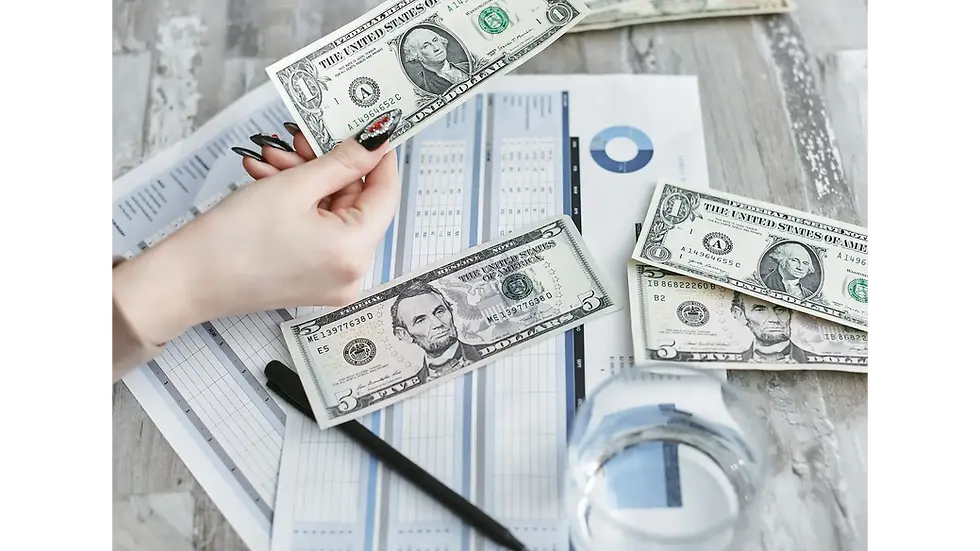 Person's hand holding cash over spreadsheets featuring various budget categories.