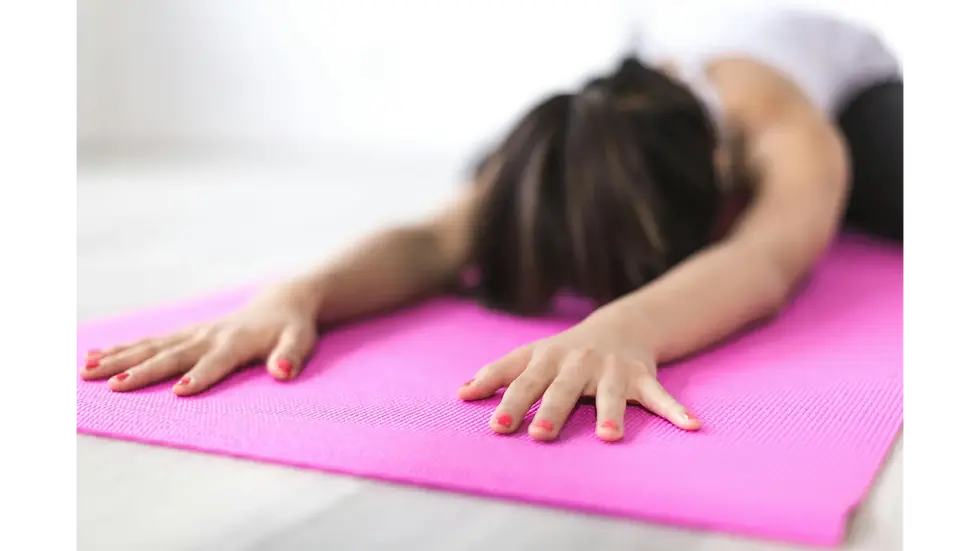 A person on a pink yoga mat stretches forward in child's pose to relax the mind and effectively reduce body stress.