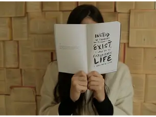 Woman covering her face with a book, reflecting on how small steps to rebuild and reset your life bring clarity