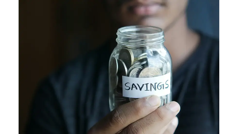 A young man holding a glass jar labeled "SAVINGS" filled with coins, highlighting smart budgeting habits in your 20s.