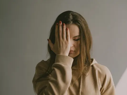 An exhausted woman covering her face, illustrating how to recognize stress to avoid severe work burnout.