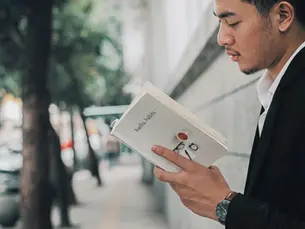Young professional reading a book on habits backed by science while walking along a quiet city sidewalk