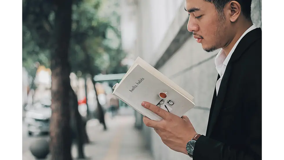 Young professional reading a book on habits backed by science while walking along a quiet city sidewalk