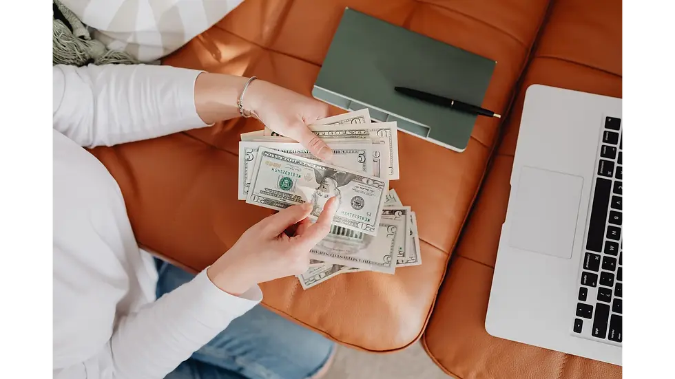 Person counting cash next to a laptop, successfully budgeting household expenses on a single income.