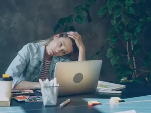 Stressed woman staring at a laptop screen at work, trying to stop procrastinating and focus on her creative design project.