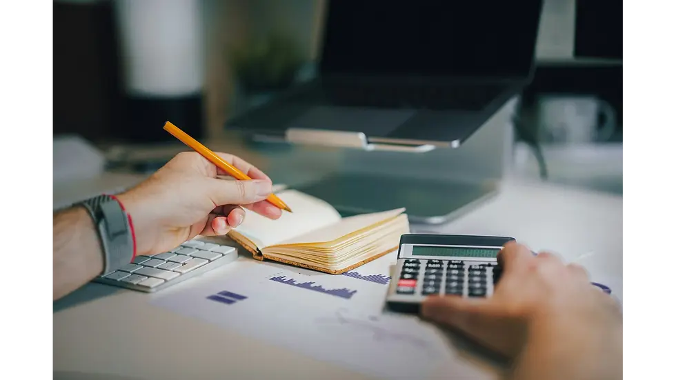 A person using a calculator and a notebook with charts on a desk, showing easy budgeting strategies helpful for beginners