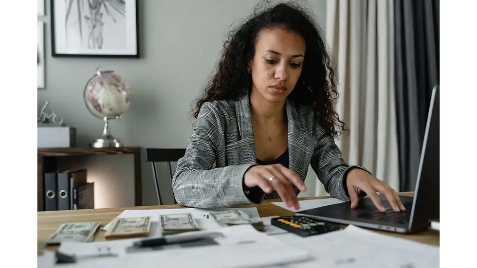 A focused woman uses a laptop and calculator to fix financial issues and create a sustainable monthly budget.