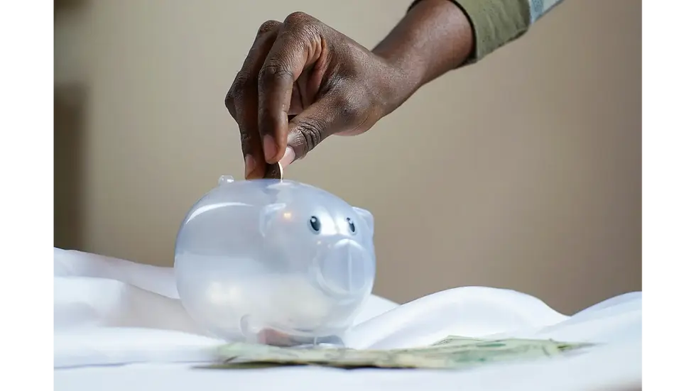 A person placing a coin into a piggy bank to wisely budget salary and grow personal savings
