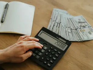 A person using a calculator and cash to manage a paycheck-to-paycheck budget with careful monthly spending plans