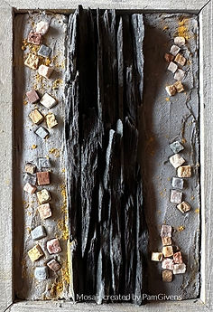 Textures of dark slate are centered on a gray surface with small colored mosaic tiles scattered around, creating a rustic, artistic composition.