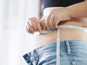 Person measuring waist with tape, wearing jeans and a crop top. The background is blurred, creating a focused and introspective mood.
