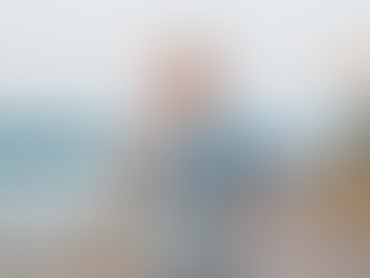 Woman jogging by a riverside path, smiling. She wears a light blue shirt, and the mood is cheerful. Blurred background with soft lighting.