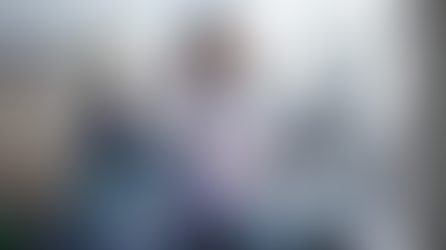 Two people exercising on ellipticals in a bright gym. A woman in a purple shirt focused on screen, man in blue shirt in background.