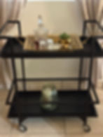 Black shelving unit with a decorative tray, glasses, decanter and small ornaments.