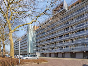 Moderne flat met lange balkons, geparkeerde auto’s en kale bomen op een zonnige dag.