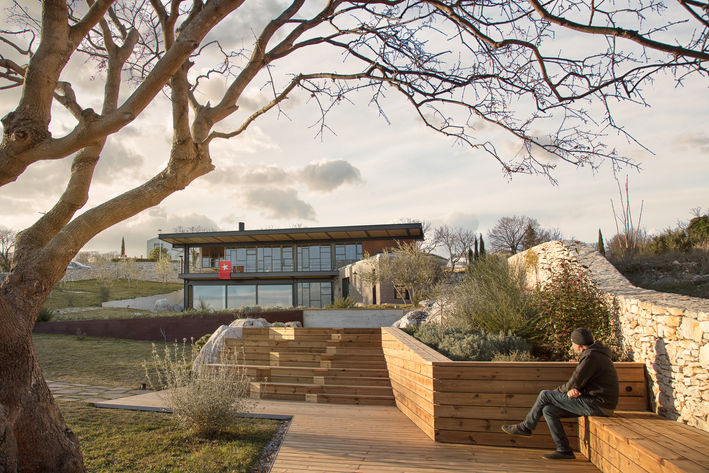 Modern house exterior in winter with a bare tree and a person sitting on a bench.