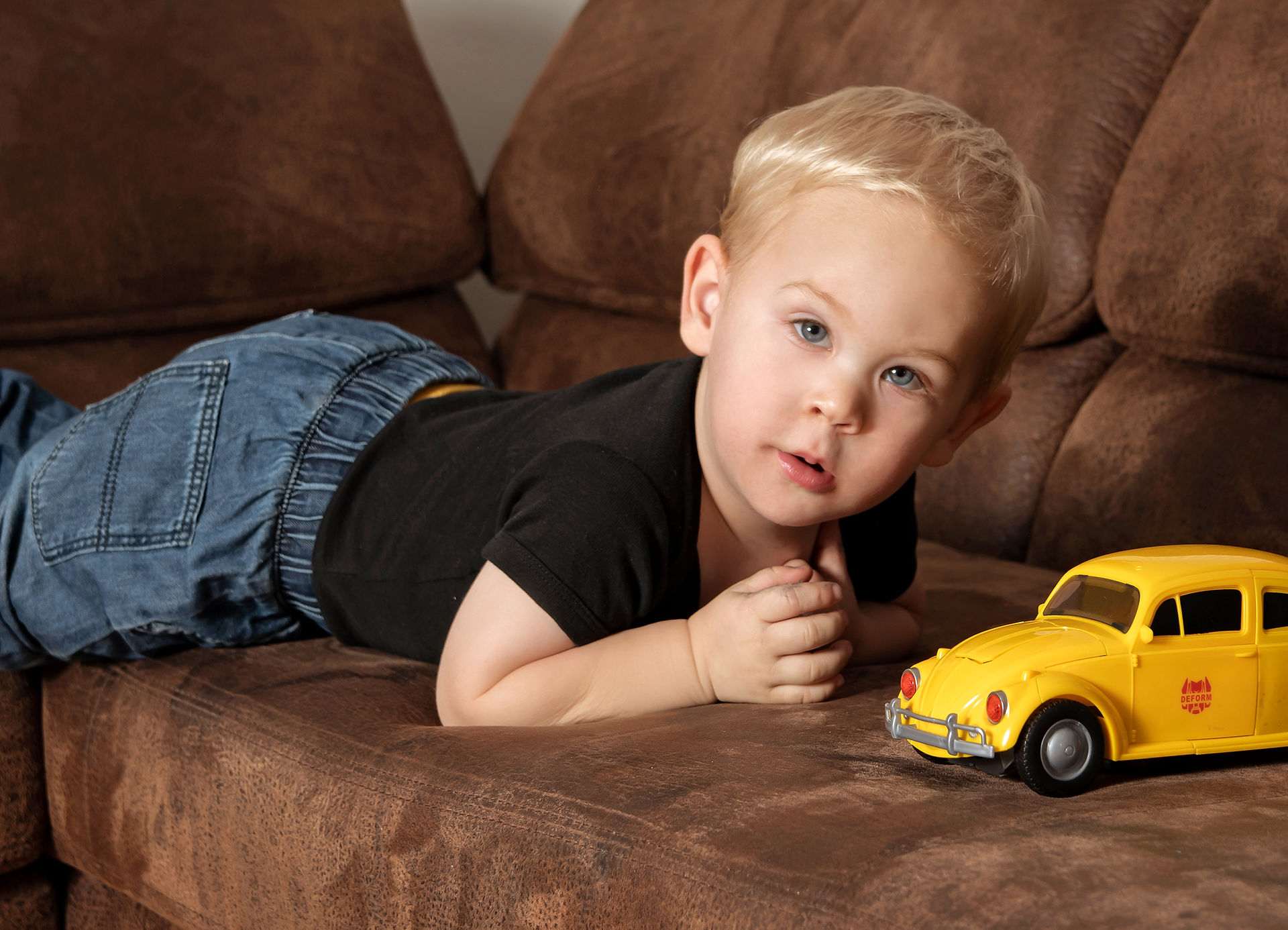 der kleinere mit einem gelben Spiele Auto auf dem Sofa