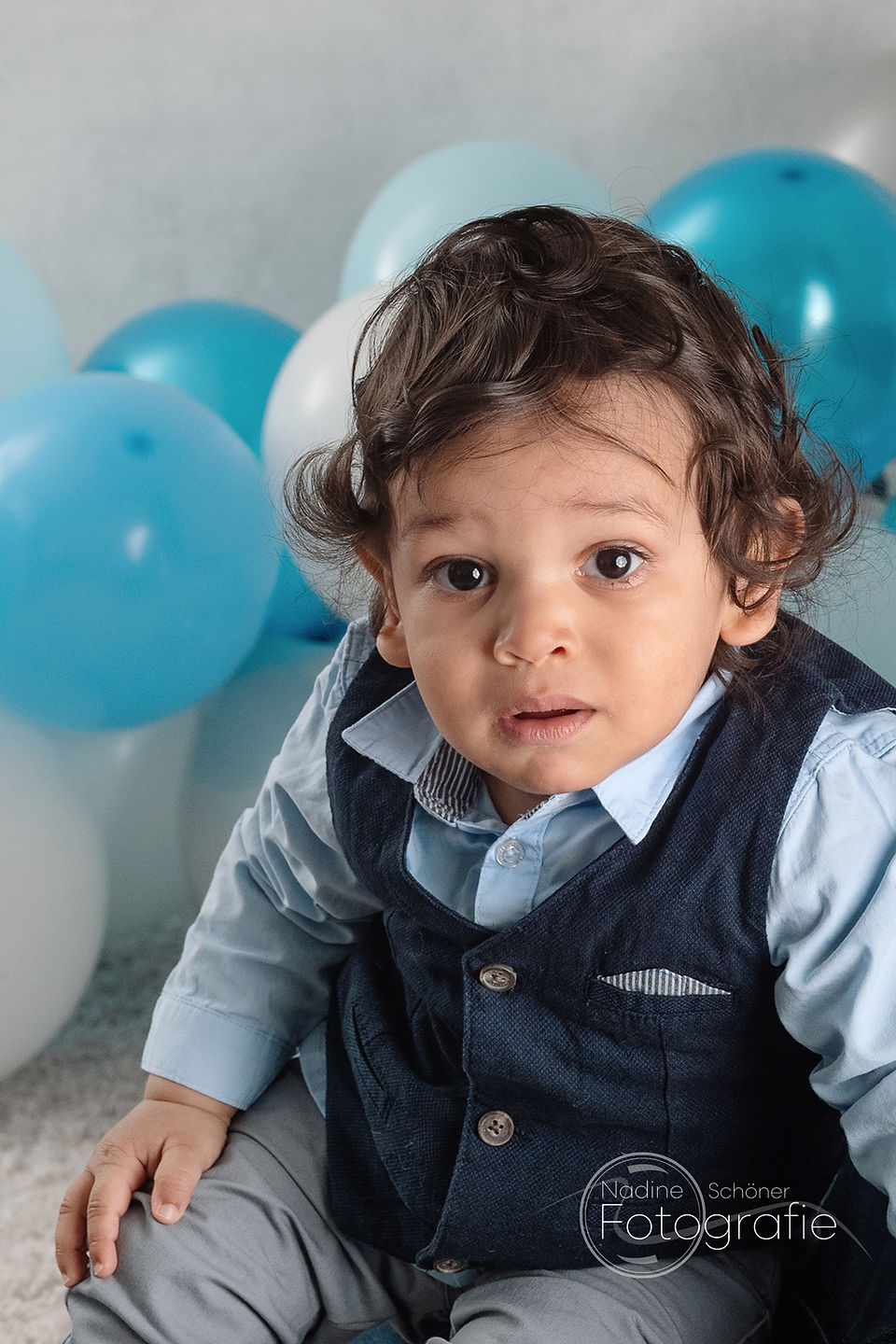 Geburtstagskind mit blauen und weißen Luftballons im Hintergrund
