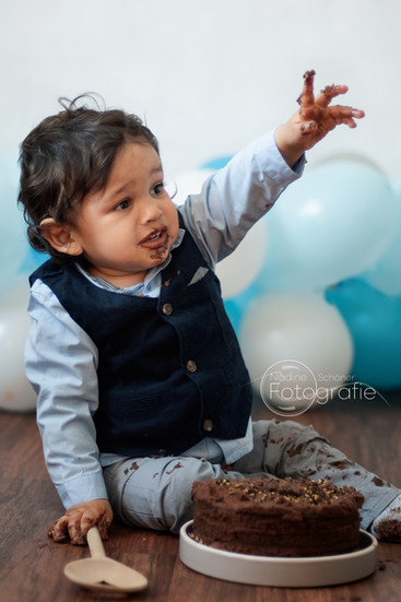 das Geburtstagskind hebt die linke Hand um den Kuchentopper zurück zu bekommen