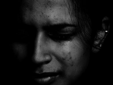 Close‑up of a girl in a dark setting with tears on her face, expressing deep sadness.