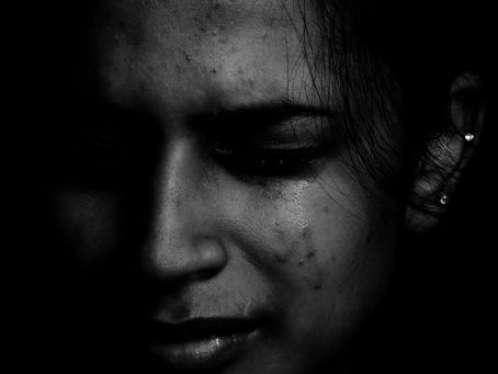 Close‑up of a girl in a dark setting with tears on her face, expressing deep sadness.