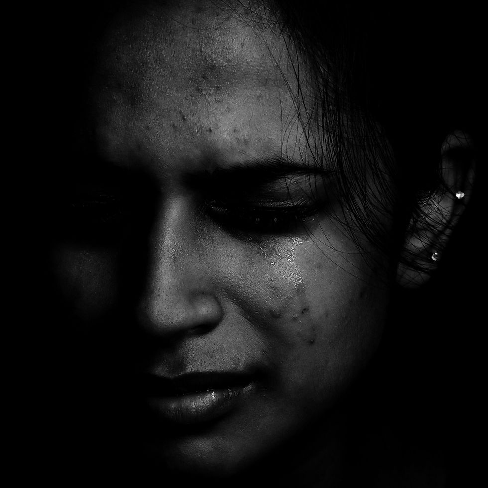Close‑up of a girl in a dark setting with tears on her face, expressing deep sadness.