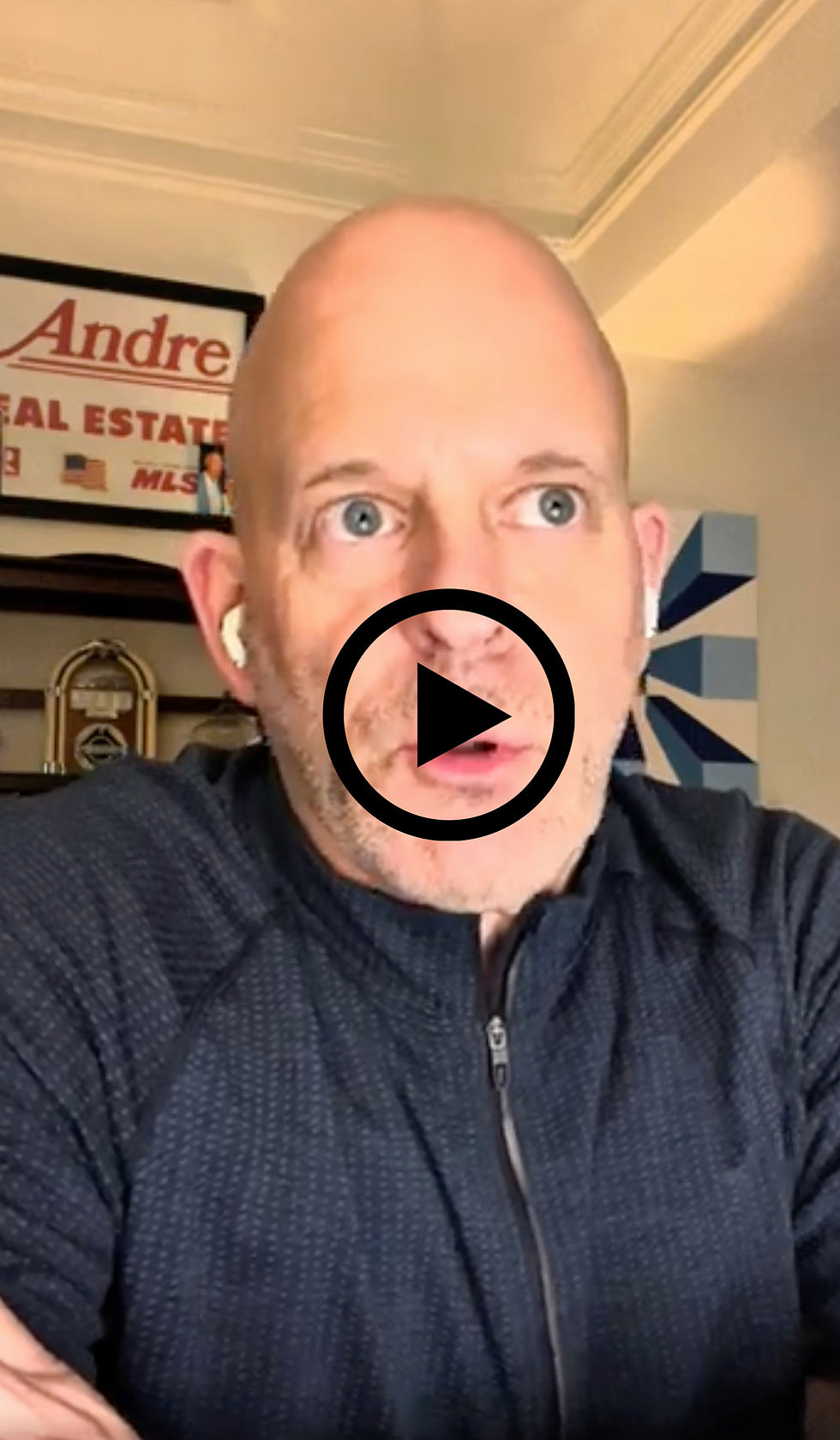 Man with earbuds looks thoughtful. Background features a "Real Estate" sign and abstract art. Warm lighting creates a contemplative mood.