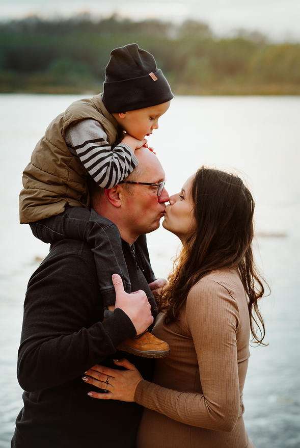 Rodzina na brzegu wisły. Rodzice dają sobie buzi  - sesja ciążowa w plenerze Warszawa