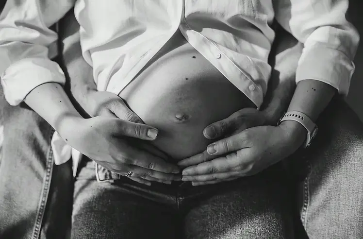 Brzuszek ciązowy z rękami rodziców  - sesja ciążowa w domu Warszawa