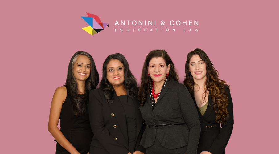 Antonini & Cohen partners, Sonal Shah, Nisha Karnani, Carolina Antonini, and Kathleen Hoyos, pose in black attire against a pink backdrop with the Antonini & Cohen Immigration Law logo above.