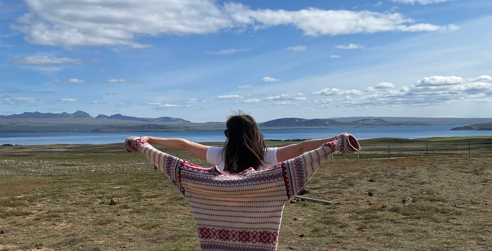 kobieta stojąca tyłem trzyma w rękach islandzki sweter, ręce ma rozpostarte