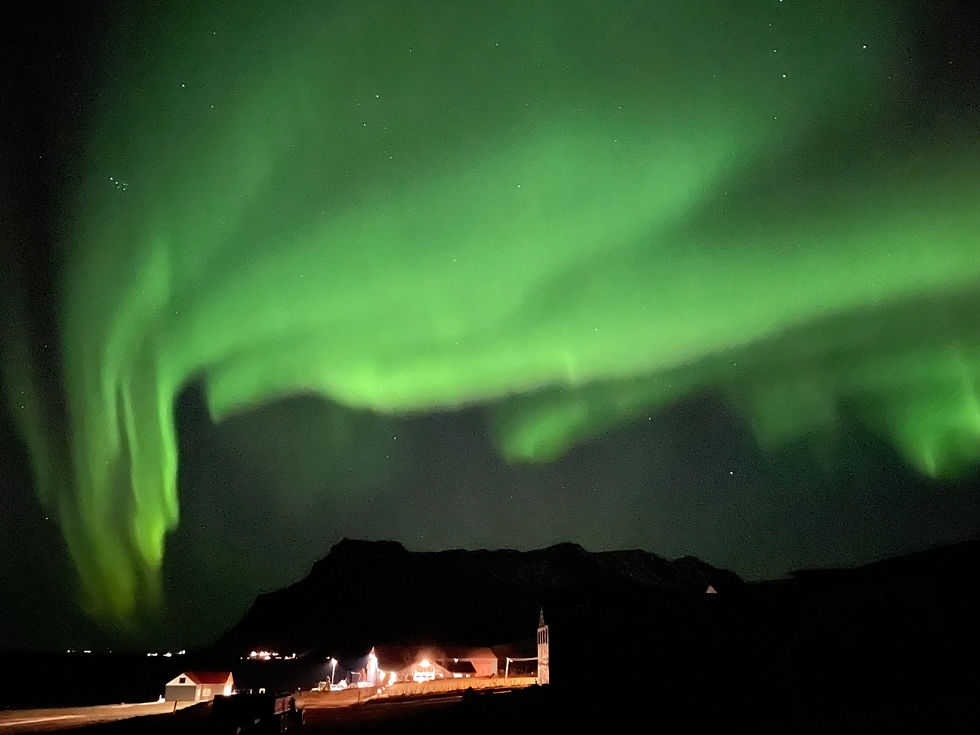 Zorza polarna nocą na Islandii nad domkami i górą
