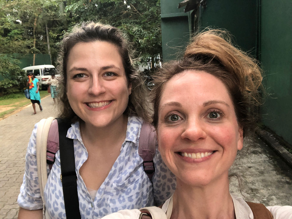 Two women smiling for a selfie. They are both wearing backpacks and there's a stone path behind them.