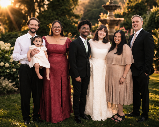 Family in formal attire with a baby in a garden with a fountain