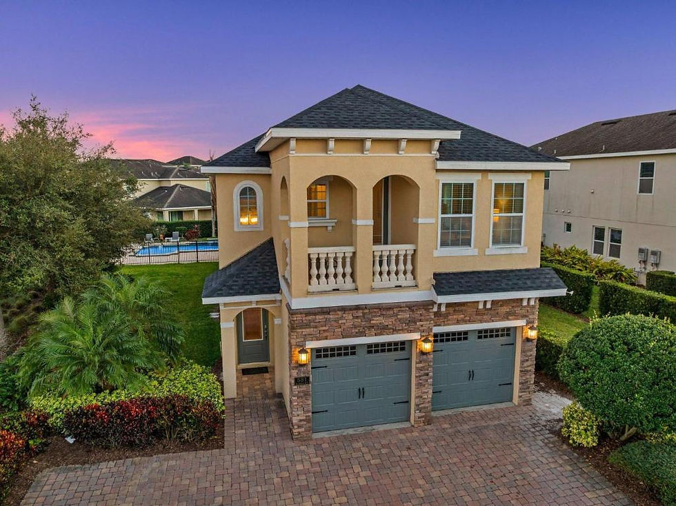 Two‑story Orlando vacation rental home with a tan exterior, stone accents, and double garage at sunset.