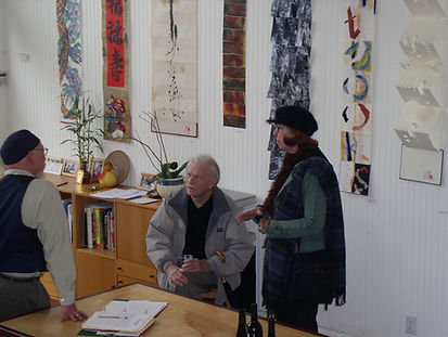 Book artist and educator Howard Munson engaging in conversation with visitors in front of accordion books displayed during a vertical art exhibition at The Drawing Works studio.