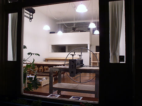 The public storefront exterior of The Drawing Works Art Studio and Press in North Beach, looking inside a brightly lit art printmaking atelier.