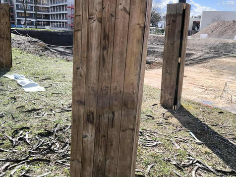 Holzpfosten im Gras stehen, Hintergrund mit Gebäuden und einem blauen Himmel.